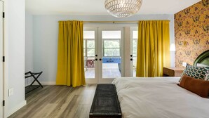 A hotel room with a bed, a bench, a desk, and a view of the outside through a door. - Riverfront Cottage in Homosassa: 'chateau Relaxo' (Homosassa)
