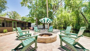 A patio with Adirondack chairs, a fire pit, and a green and white umbrella. - Riverfront Cottage in Homosassa: 'chateau Relaxo' (Homosassa)