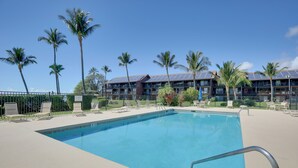 A swimming pool with lounge chairs and palm trees, surrounded by a building with solar panels. - Molokai Shores Resort Condo w/ Pool & Views! (Kaunakakai)
