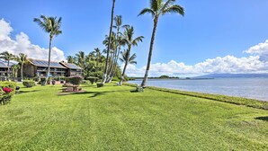 A well-maintained lawn with palm trees, a pool, and a building with solar panels. - Molokai Shores Resort Condo w/ Pool & Views! (Kaunakakai)