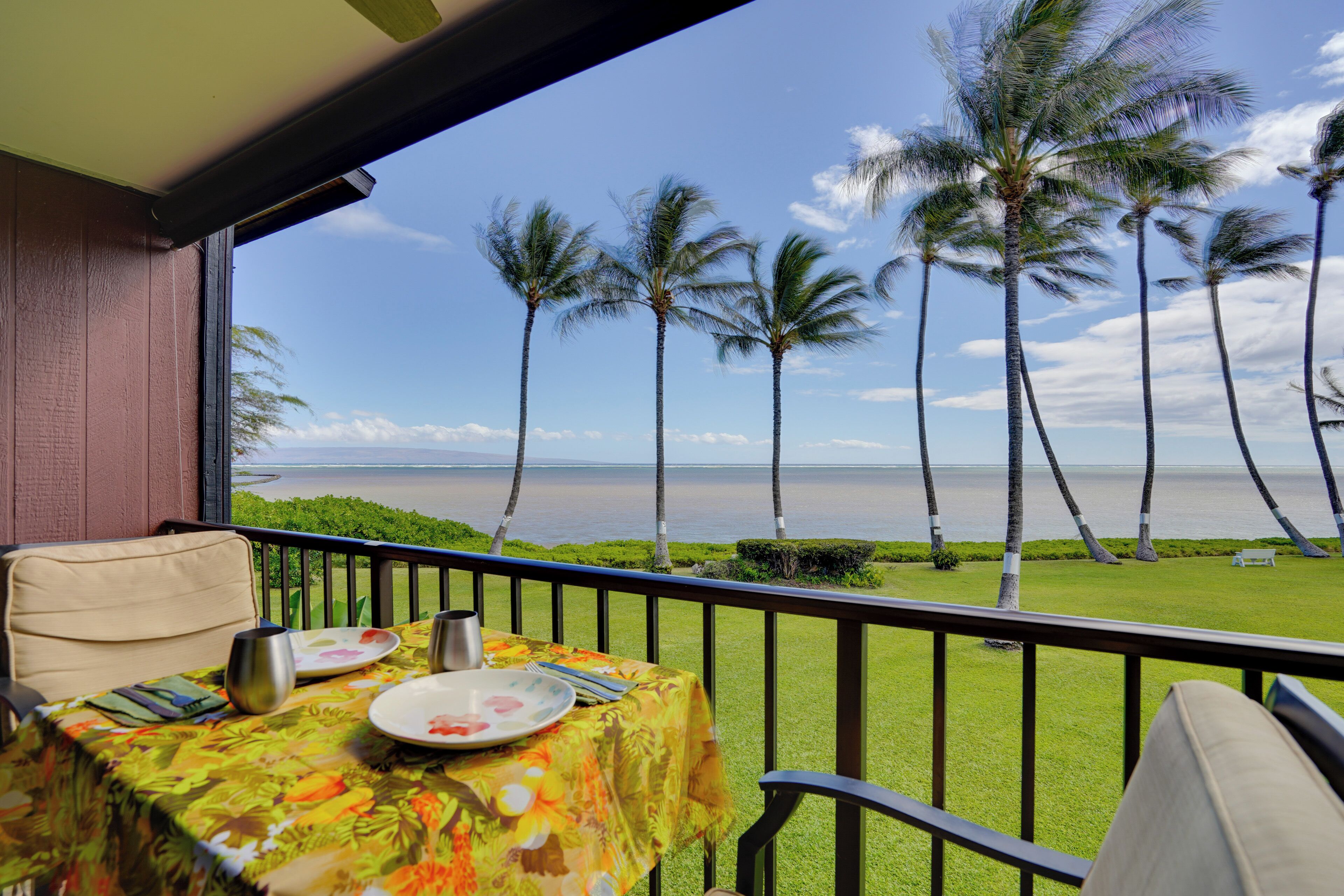 Un balcon avec une table dressée pour le dîner, donnant sur une plage bordée de palmiers et sur l’océan.