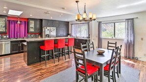 A modern kitchen with dark cabinets, a central island with red chairs, a dining table with chairs, and a chandelier. - Vibrant Weaverville Escape w/ Deck & Creek! (Weaverville)
