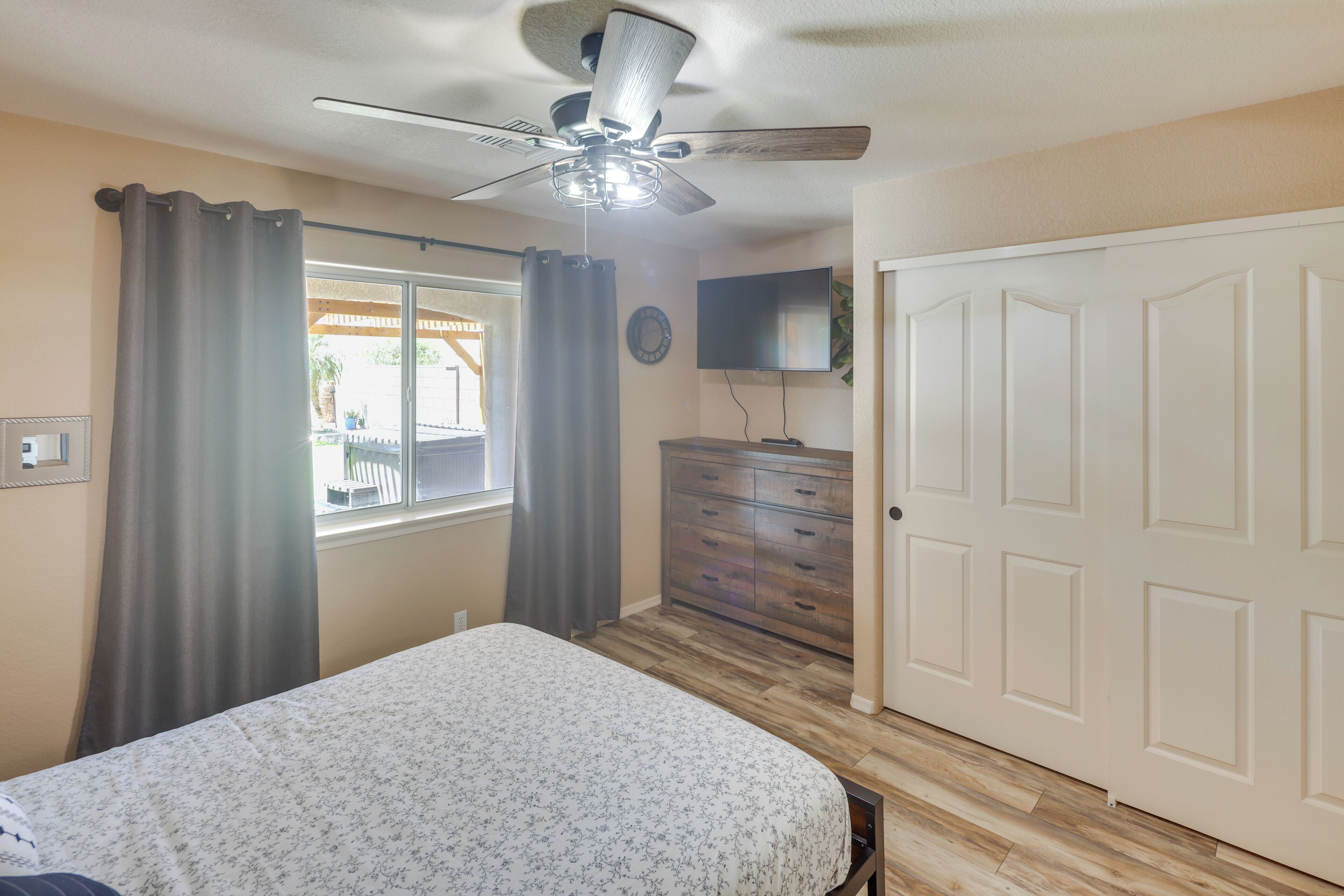 A bedroom with a bed, a ceiling fan, a dresser, a TV, and a door.