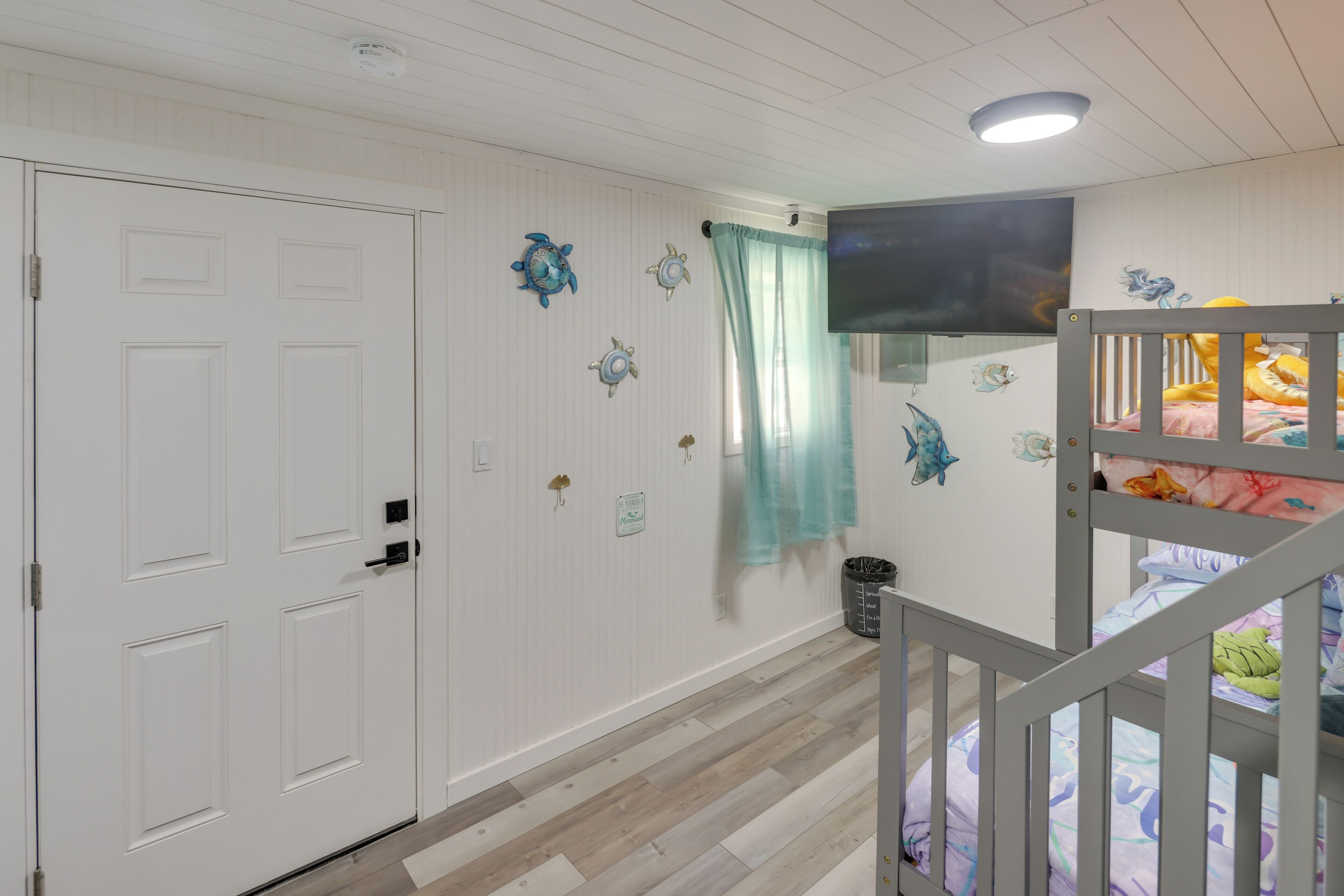 A child's bedroom with a bunk bed, white walls, and decorative fish wall art.