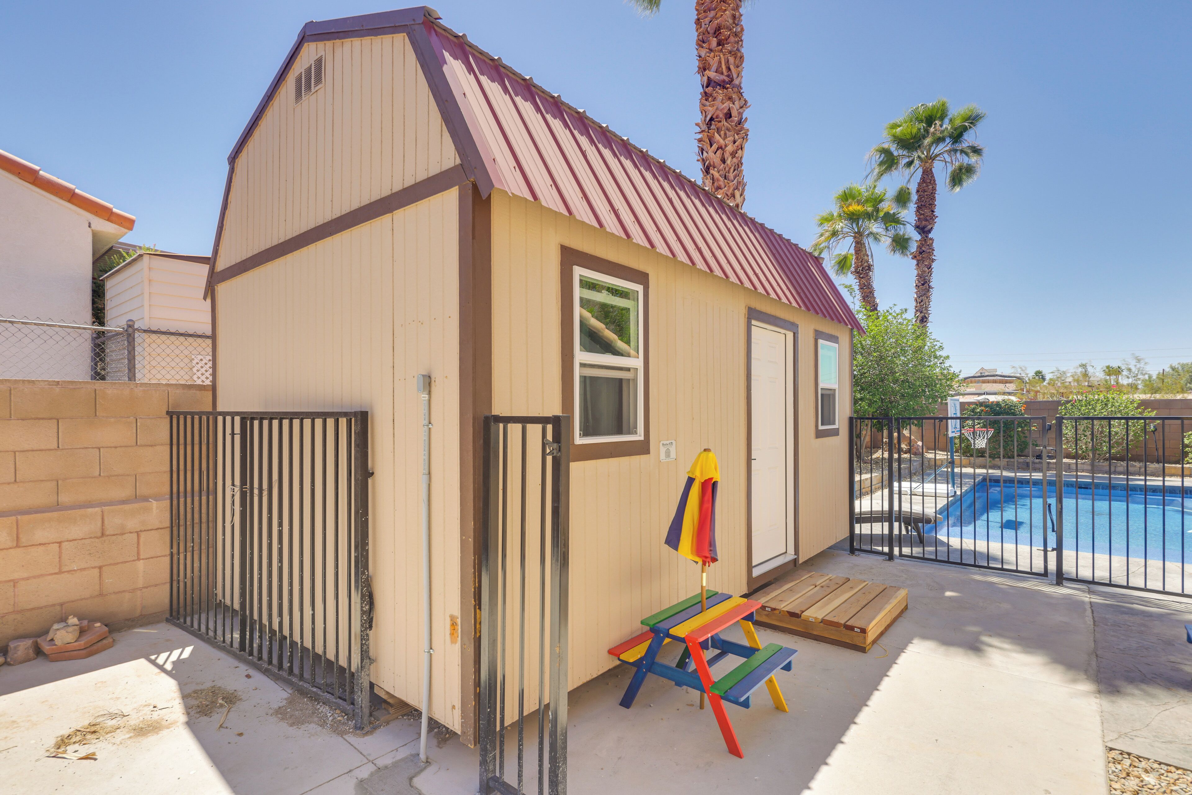 A small, single-story building with a metal roof, a fenced patio area, and a pool.