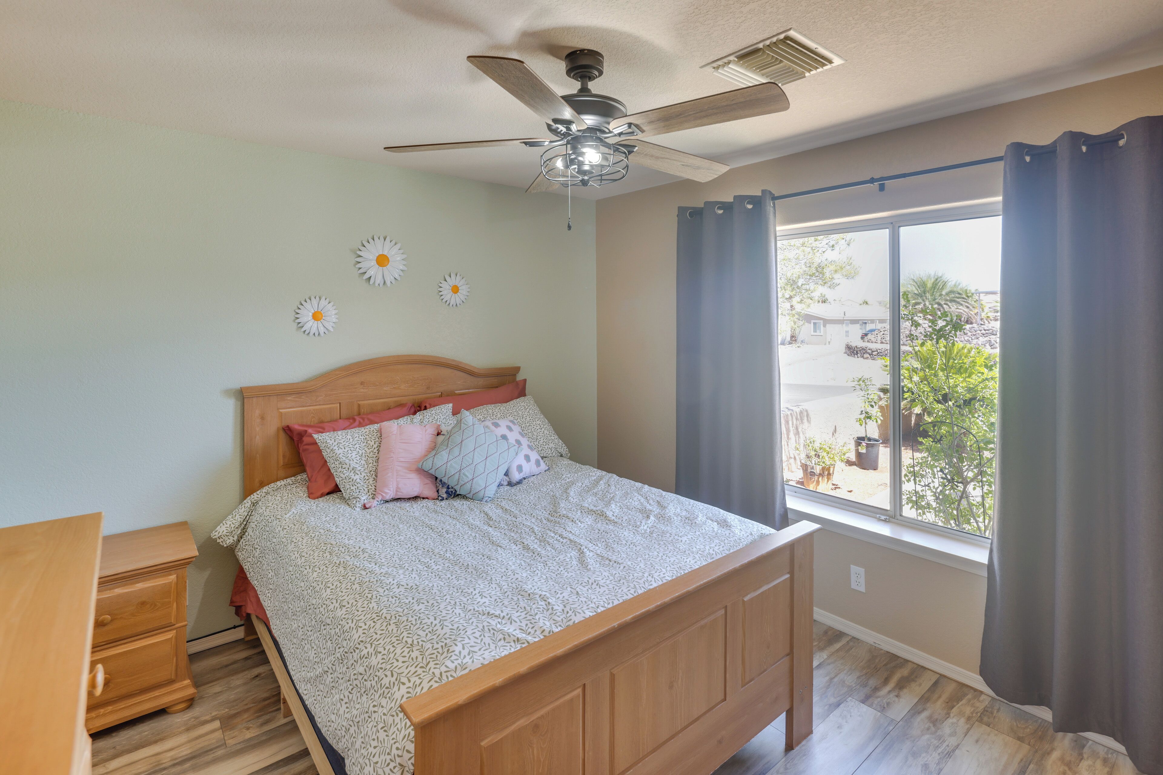 A bedroom with a wooden bed, a nightstand, a ceiling fan, and a large window with curtains.
