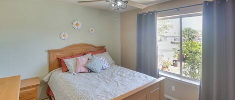 A bedroom with a wooden bed, a nightstand, a ceiling fan, and a large window with curtains.