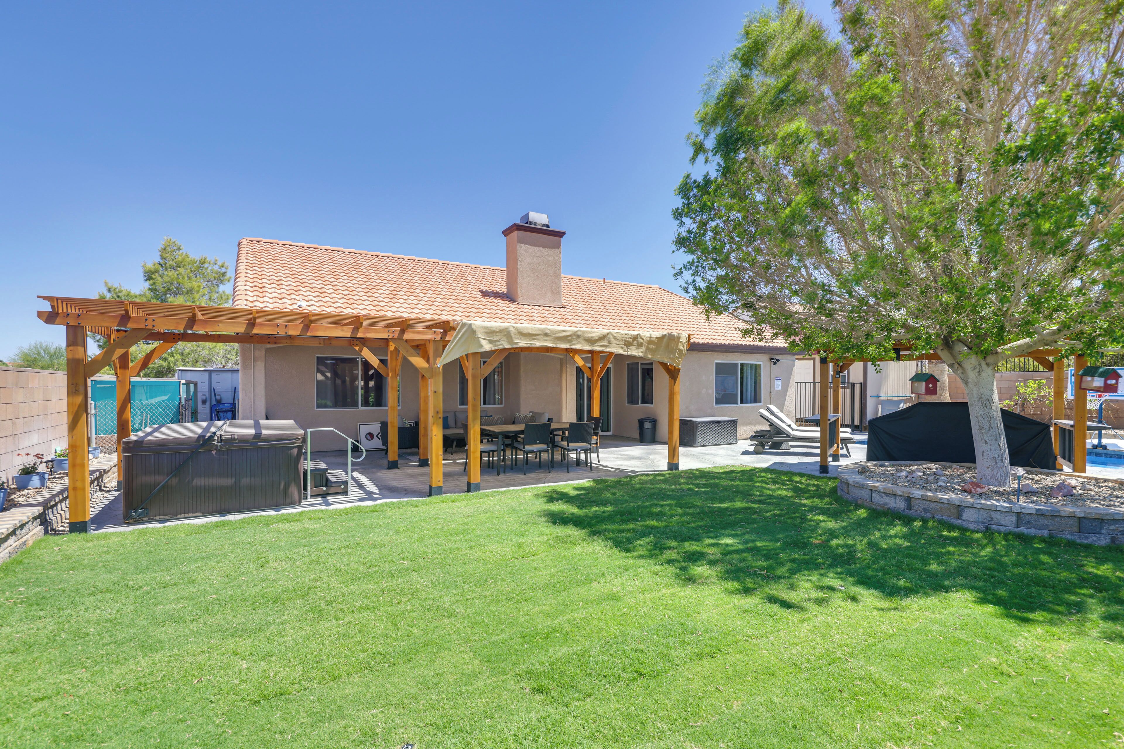 Un patio trasero con una pérgola, zona de barbacoa y un árbol.