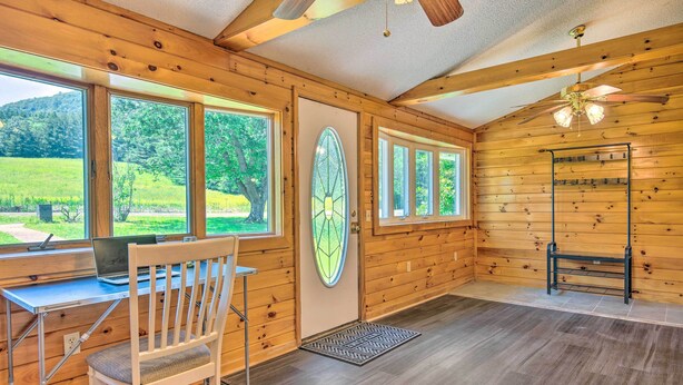 L’intérieur d’une cabane en bois, avec un bureau, une chaise et de grandes fenêtres donnant sur un paysage verdoyant.