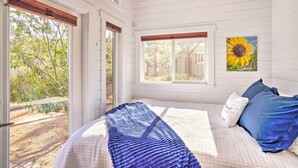 Une chambre à coucher avec un lit, une fenêtre donnant sur un paysage verdoyant et un tableau représentant un tournesol accroché au mur.
