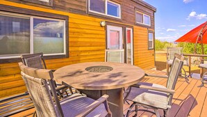 Une terrasse en bois avec une table ronde et des chaises, un foyer et un espace salon abrité.