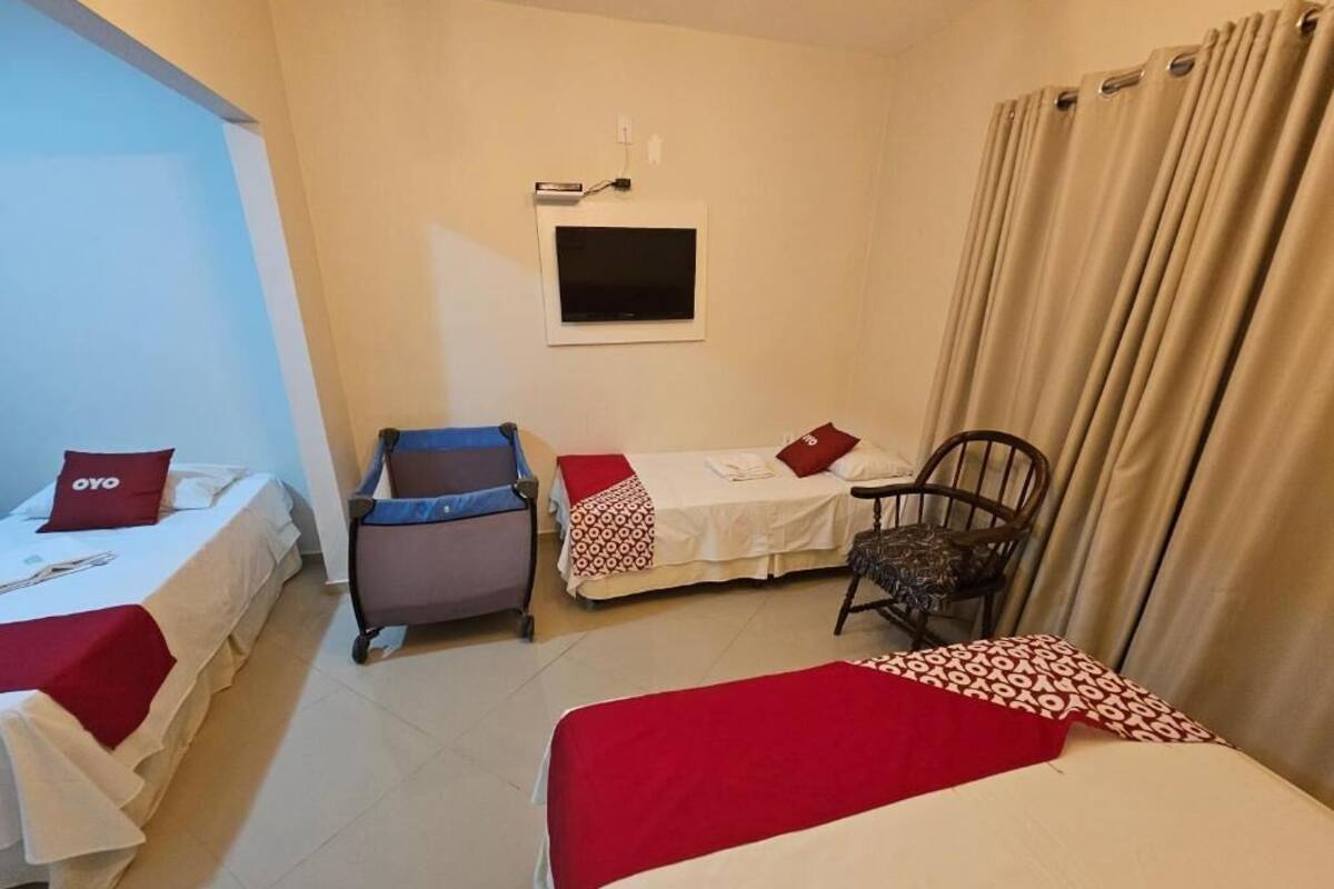 A hotel room with two beds, a desk, a chair, a TV, and a window with curtains.