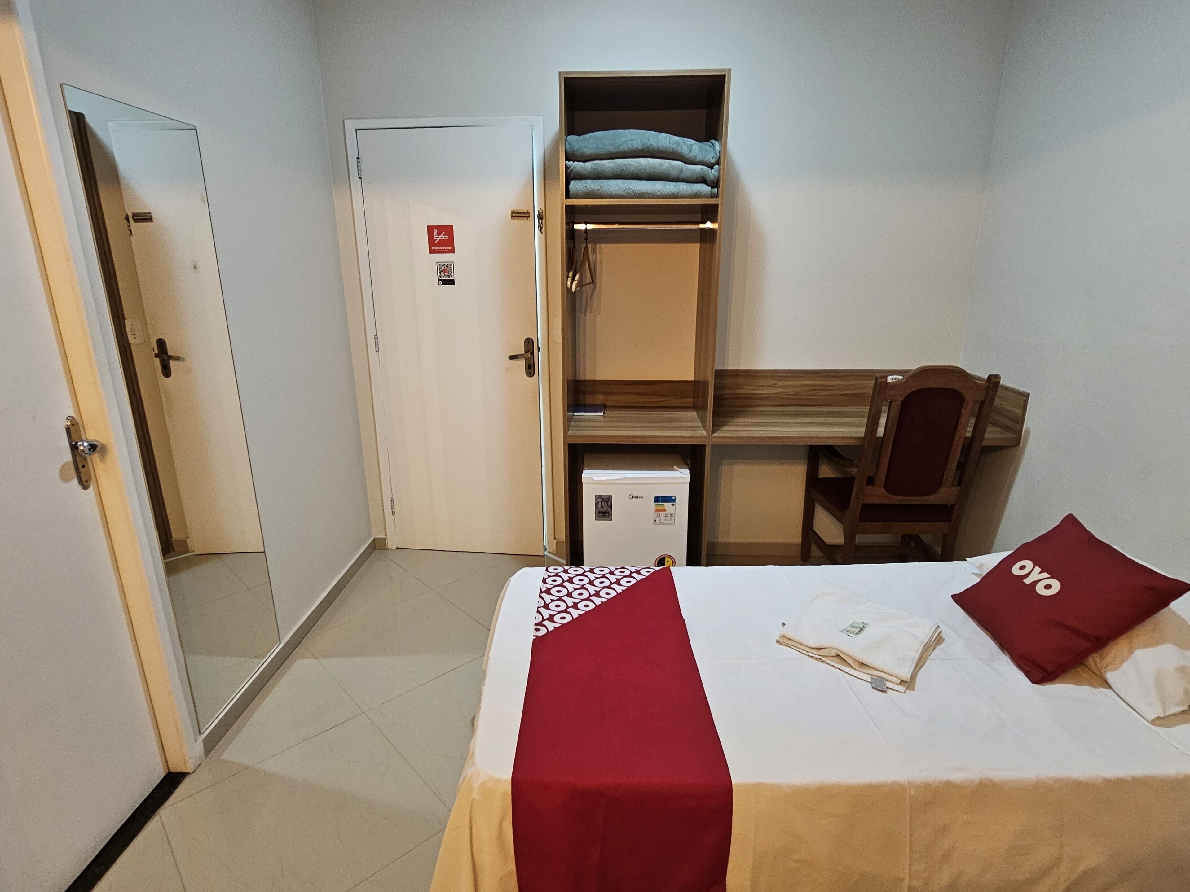 A hotel room with a bed, a desk, a chair, a wardrobe, and a door.