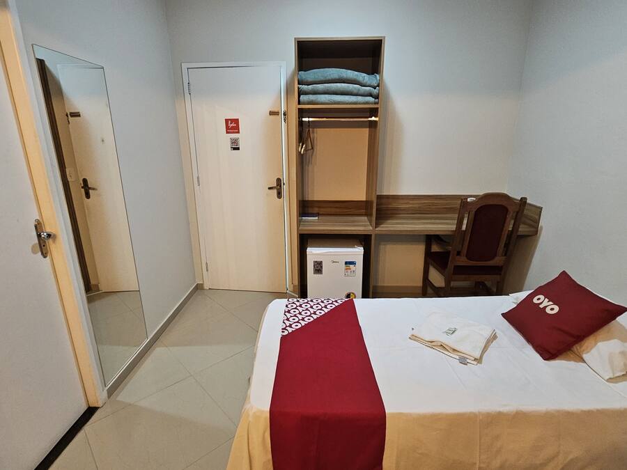 A hotel room with a bed, a desk, a chair, a wardrobe, and a door.