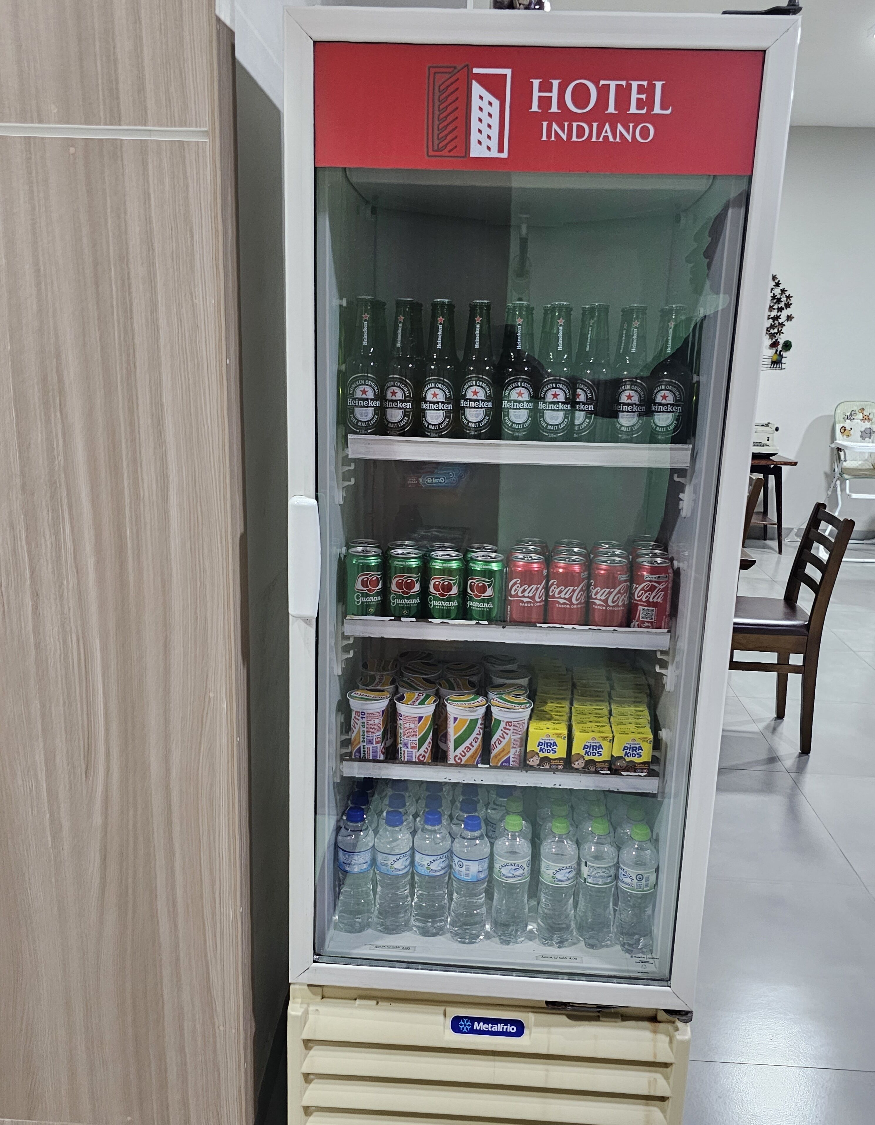 A hotel refrigerator stocked with beverages including Heineken beer, Coca-Cola, and Pira Kos juice.