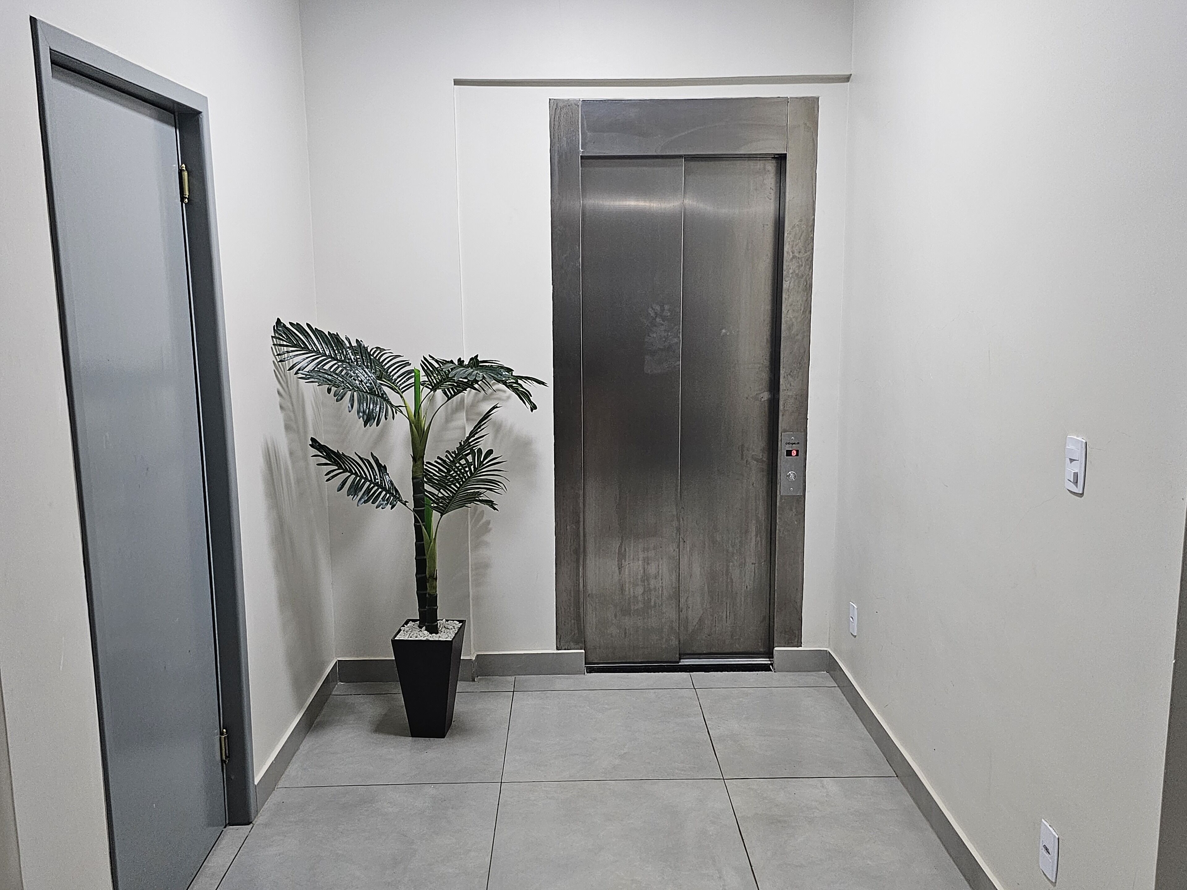 Un pasillo con una planta en maceta, una puerta de ascensor cerrada y una puerta a la izquierda.