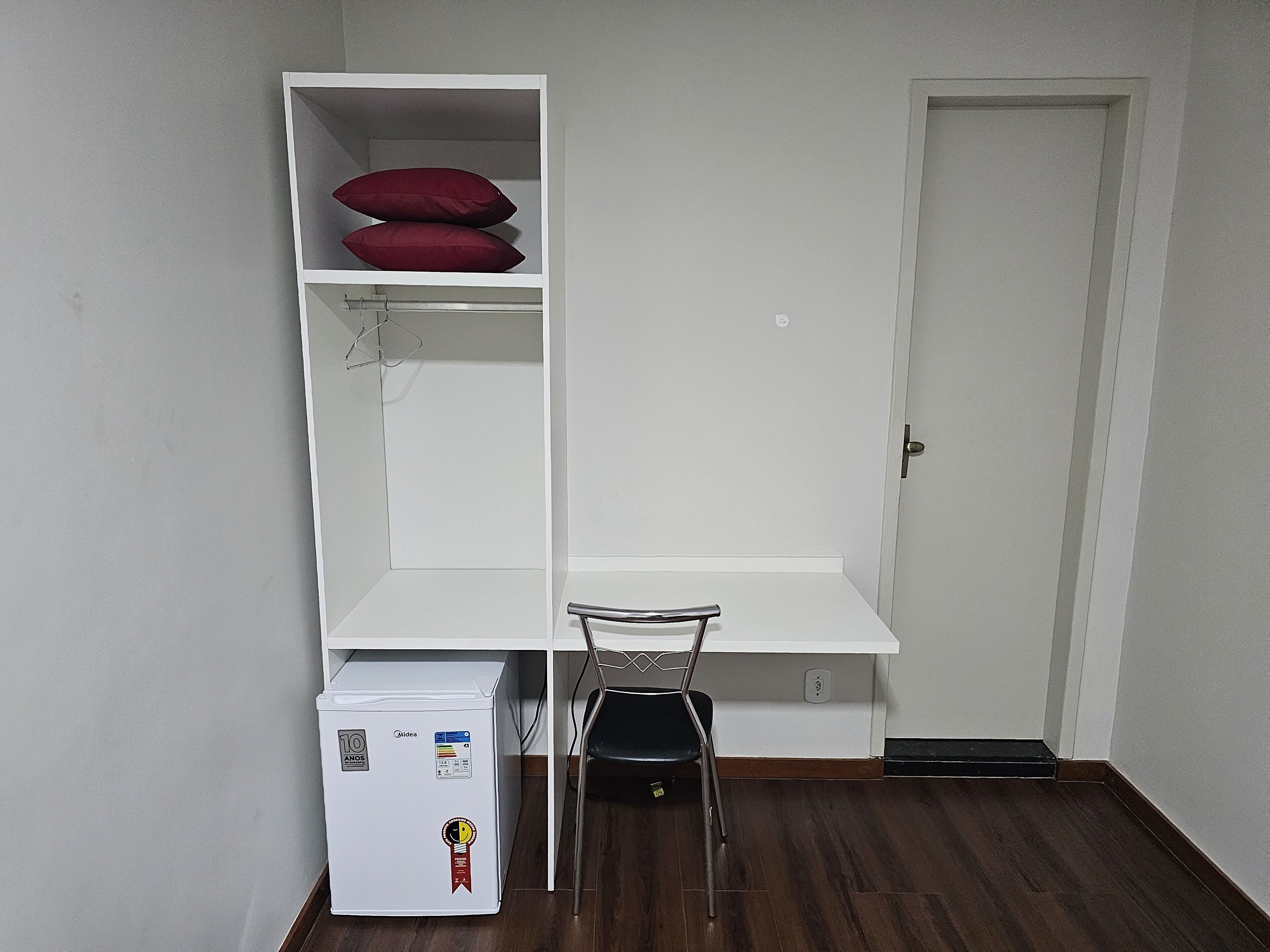 Een kleine kamer met een wit bureau, een kleine koelkast en een deur.