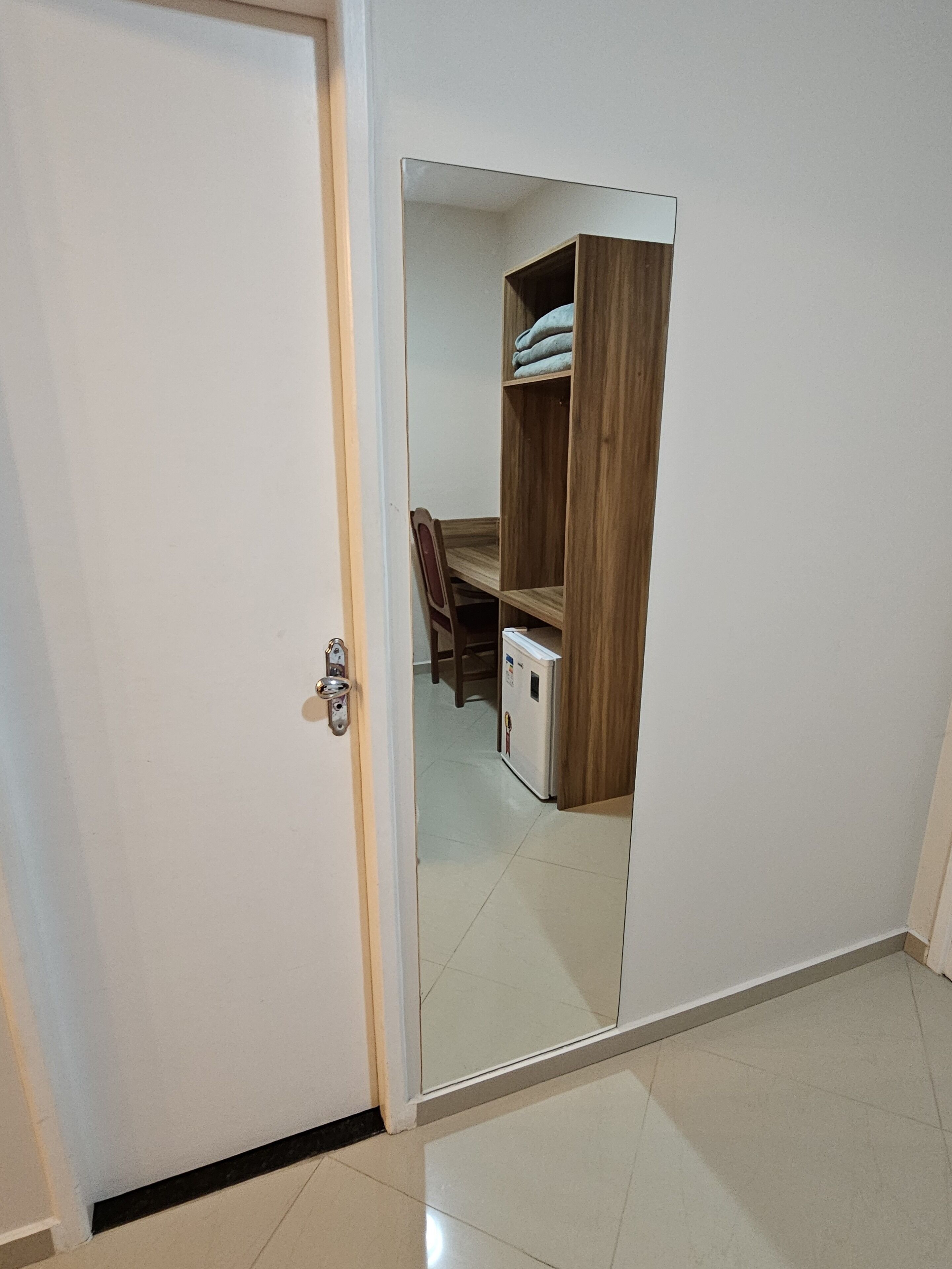 Una habitación con una puerta blanca, un armario de madera y un pequeño electrodoméstico blanco, probablemente un refrigerador o calefactor.
