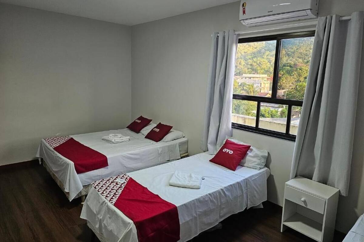 A hotel room with two single beds, a small white nightstand, and a window with curtains.