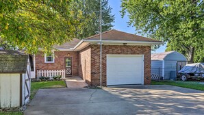 A single-story brick house with a white garage door, a small front porch, and a covered trailer in the driveway. - Lakefront Cottage w/ Fishing & Private Yard! (Port Clinton)