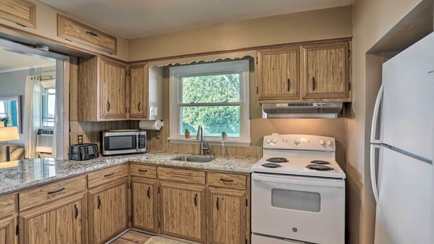 A kitchen with wooden cabinets, a microwave, a stove, and a refrigerator. - Lakefront Cottage w/ Fishing & Private Yard! (Port Clinton)