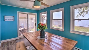 A room with teal walls, a wooden table, a ceiling fan, and a view of the outdoors. - Lakefront Cottage w/ Fishing & Private Yard! (Port Clinton)