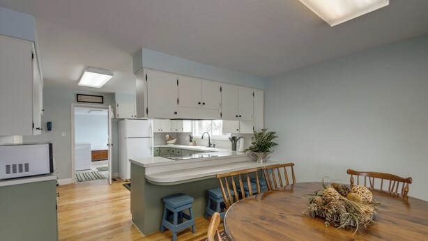 A modern kitchen with white cabinets, a central island, and a dining area with a wooden table and chairs. - Burley Home w/ Playground - 1 Mi to Golf Course! (Burley)
