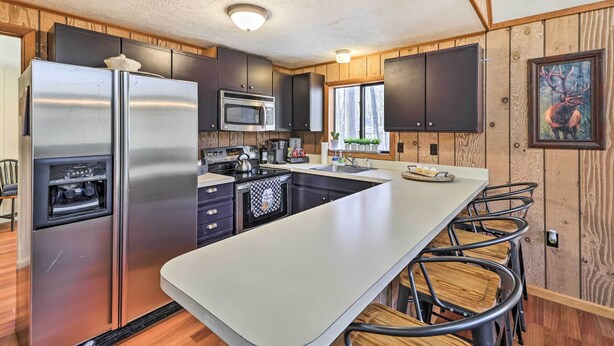 A modern kitchen with stainless steel appliances, wooden cabinetry, and a central island with bar stools. - Fire Pit & Grill: 'woodside Nest' in Pocono Lake! (Pocono Lake)