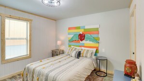 Une chambre avec un lit, une œuvre d’art murale aux couleurs vives, une petite table et une batterie.