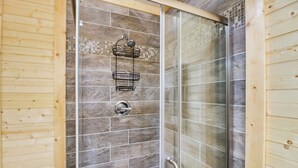 Une douche avec une porte en verre, un revêtement mural en bois et un porte-serviettes en métal.