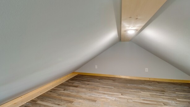 Une pièce avec un plafond en pente, un plancher en bois et des murs de couleur gris clair.