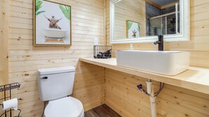 Une salle de bain aux murs lambrissés, équipée de toilettes, d’un lavabo et d’un miroir.