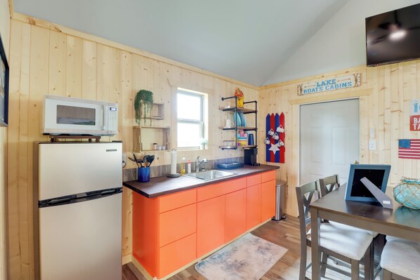 A kitchen with wooden walls, a white refrigerator, an orange countertop, a sink, and a dining table with chairs. - Beautiful Studio Cabin Near Greers Ferry Lake! (Higden)