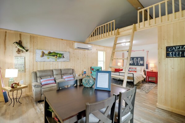 A cozy cabin interior with a dining area, a sofa, a ladder, and a sign reading "CAPTAIN QUARTER KEEP". - Beautiful Studio Cabin Near Greers Ferry Lake! (Higden)