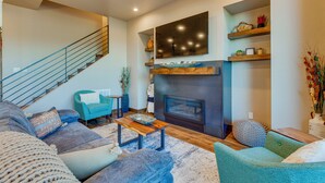 A modern living room with a fireplace, a staircase, and a seating area with sofas and a coffee table. - Angel Fire Home w/ Hot Tub < 1 Mi to Ski Slopes! (Angel Fire)
