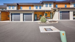 A modern multi-story building with multiple garage doors, a small landscaped area with a tree, and a storm drain. - Angel Fire Home w/ Hot Tub < 1 Mi to Ski Slopes! (Angel Fire)