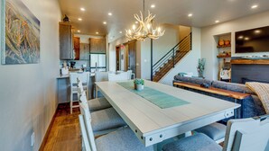 A modern kitchen with white cabinetry, a dining area with a long table and chairs, and a staircase leading to a lofted living area. - Angel Fire Home w/ Hot Tub < 1 Mi to Ski Slopes! (Angel Fire)