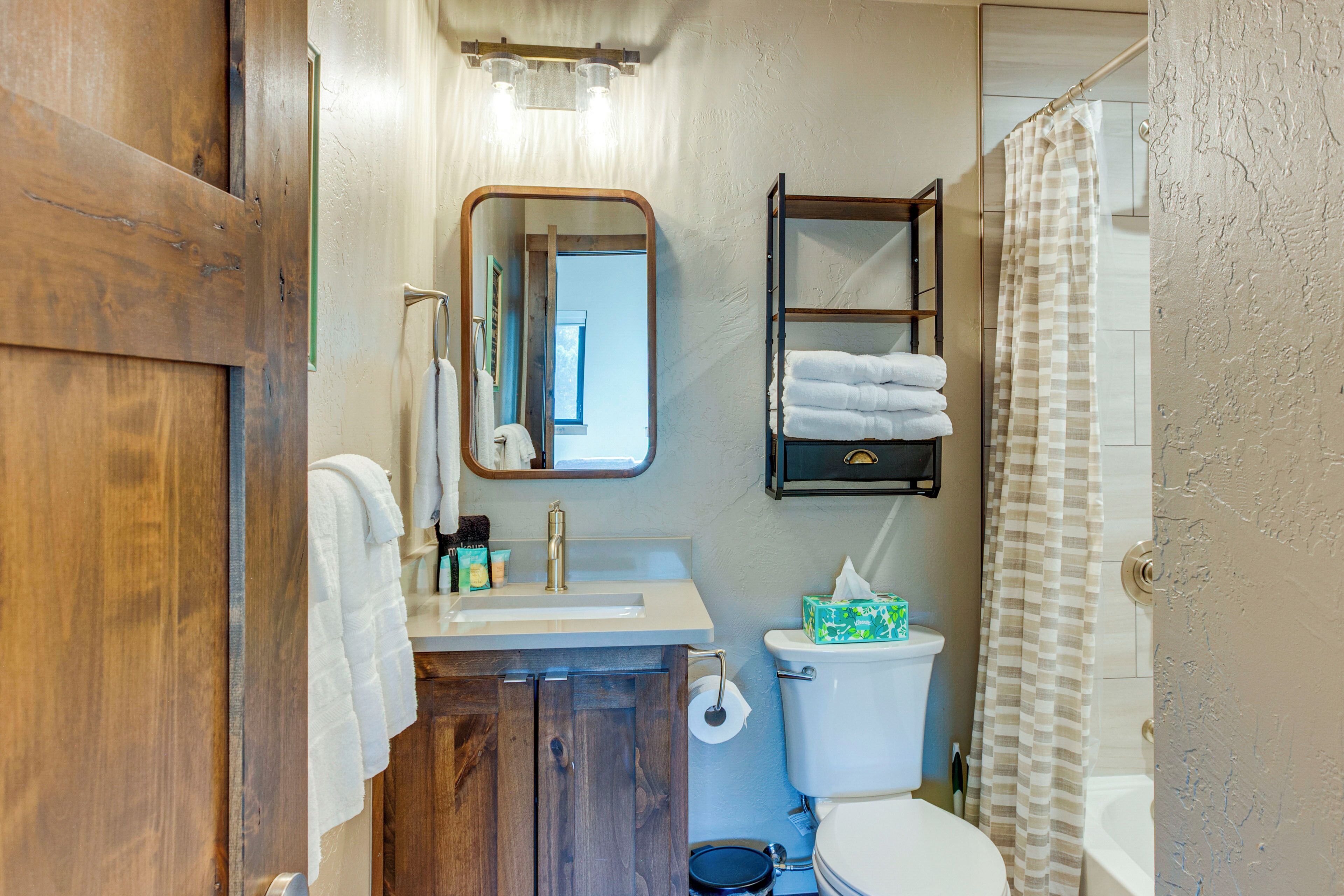 A bathroom with a wooden door, a white sink, a mirror, a towel rack, a toilet, and a shower curtain.