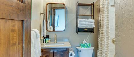 A bathroom with a wooden door, a white sink, a mirror, a towel rack, a toilet, and a shower curtain.