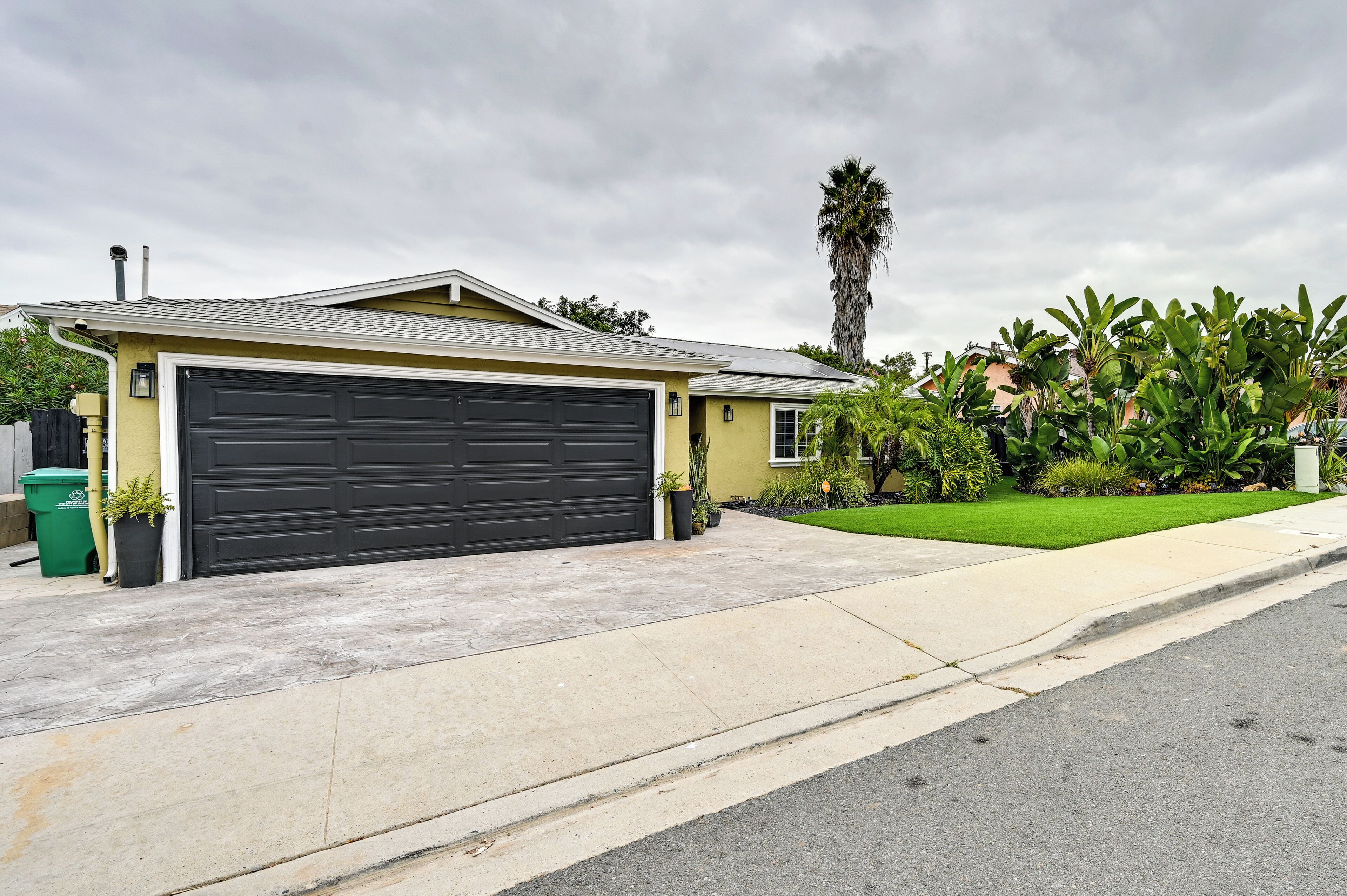 A residential garage with a dark door, a driveway, and a well-maintained lawn with palm trees.