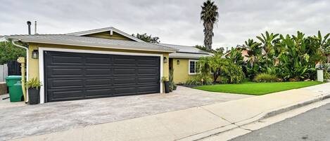 A residential garage with a dark door, a driveway, and a well-maintained lawn with palm trees.