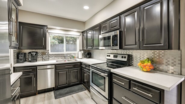 Una cocina moderna con electrodomésticos de acero inoxidable, muebles oscuros y salpicadero de azulejos.