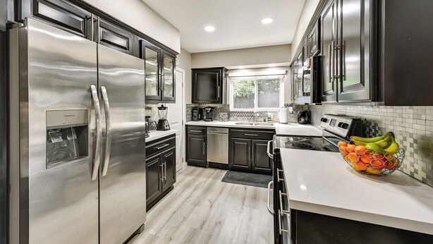 A modern kitchen with stainless steel appliances, dark cabinetry, and a white countertop.