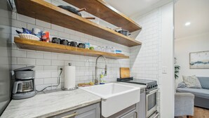 A kitchen with a white sink, a coffee maker, and wooden shelves above.