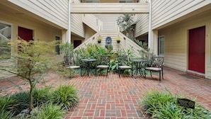 A courtyard with a brick floor, outdoor seating, and a staircase leading to an upper level.