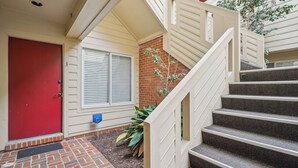 A red door, a white window with blinds, a brick wall, and a staircase with a handrail.