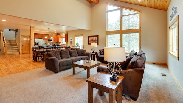 A spacious living room with a wooden ceiling, a large window, a sofa, a coffee table, and a kitchen in the background. - Sunriver Group Getaway: Explore Deschutes Forest! (Bend)