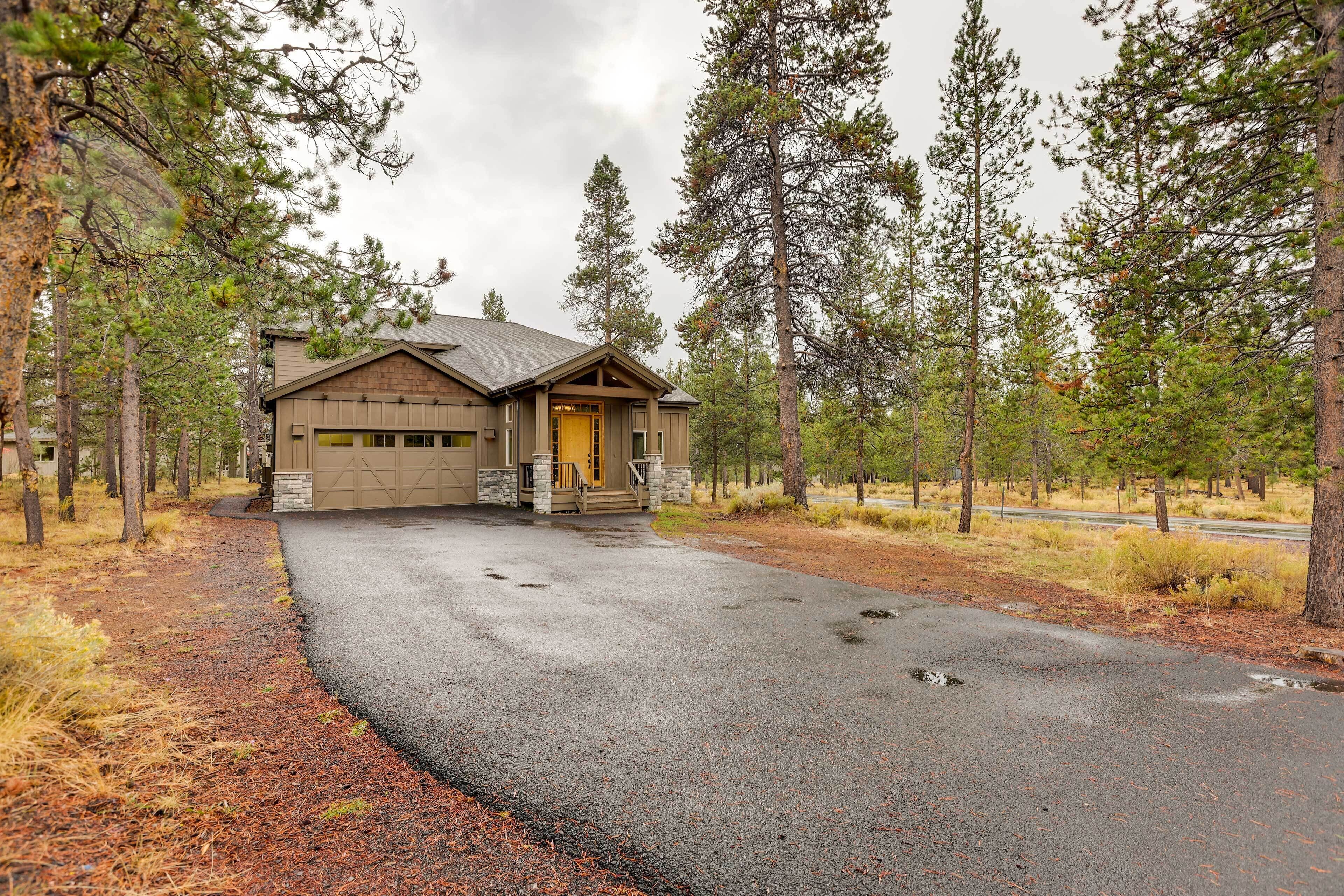 A two-story house with a garage, surrounded by tall pine trees.