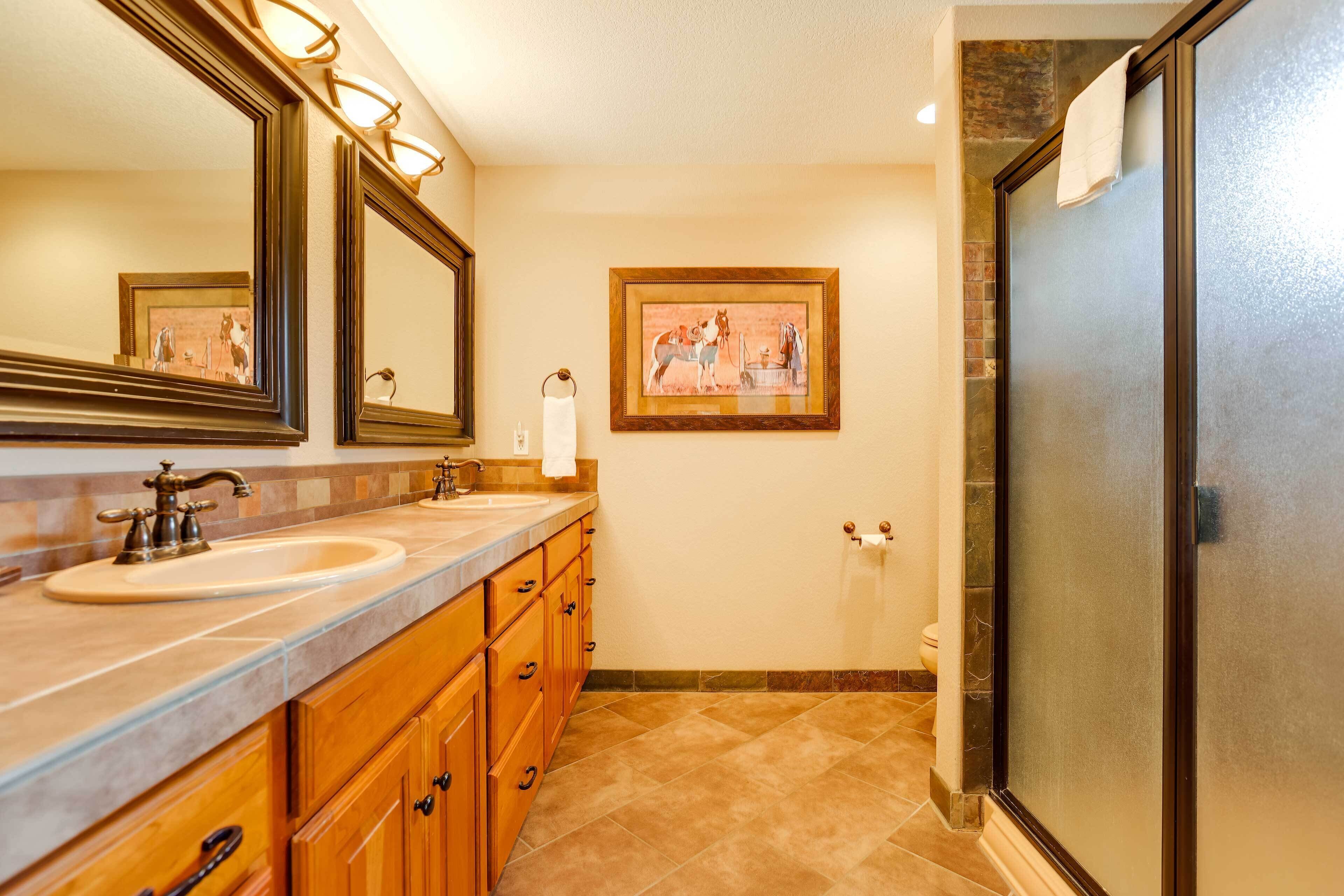 A bathroom with two sinks, wooden cabinets, a large mirror, a framed picture on the wall, and a shower with a glass door.