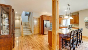 A spacious kitchen with wooden flooring, a central island with bar stools, and a stainless steel refrigerator. - Sunriver Group Getaway: Explore Deschutes Forest! (Bend)